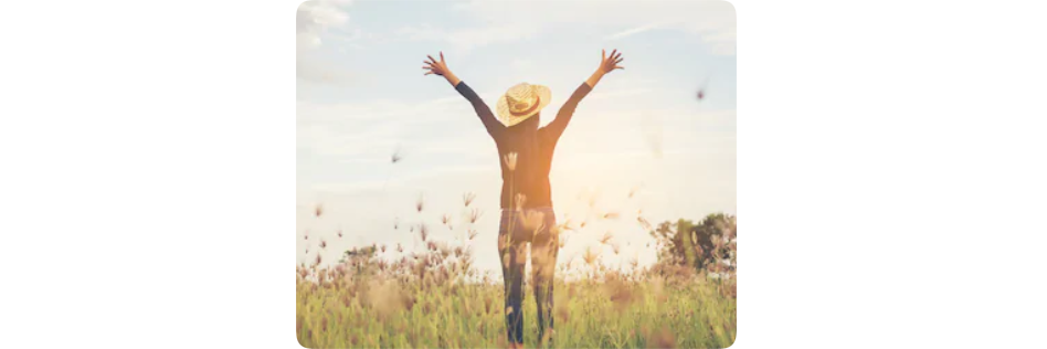 Woman standing triumphantly in a meadow with her arms raised to the sky in celebration
